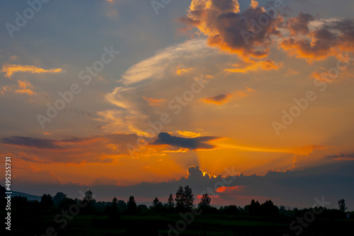 Sunset, clouds lit by the orange rays of the sun against the blue evening sky. Colorful summer landscape.