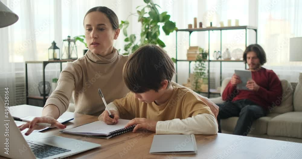 Mother helping son doing homework using laptop and father using digital tablet at home Mother helping son doing homework using laptop and father using digital tablet at home