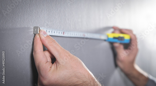 Man measures a gray wall with measuring tape.