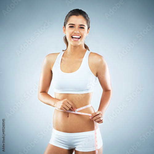 Feels great to be getting closer to my goals. Studio portrait of an attractive young woman measuring her waist against a grey background. © Nola V/peopleimages.com