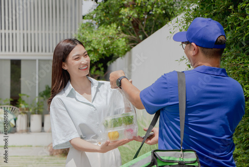 Delivery man delivering food to a beautiful Asian girl in front of the house.