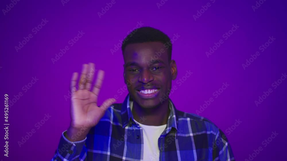 Happy African Guy Waving Hand Gesturing Hello Over Purple Background Happy African Guy Waving Hand Gesturing Hello Over Purple Background