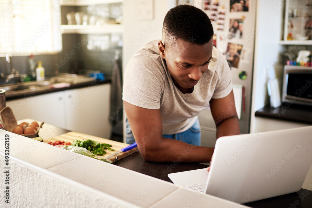 Lets check out some new recipes. Cropped shot of a handsome young man using a digital tablet while making breakfast in his kitchen at home. Lets check out some new recipes. Cropped shot of a handsome young man using a digital tablet while making breakfast in his kitchen at home.