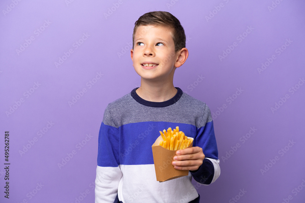 Little boy holding fried chips isolated on purple background thinking an idea while looking up Little boy holding fried chips isolated on purple background thinking an idea while looking up