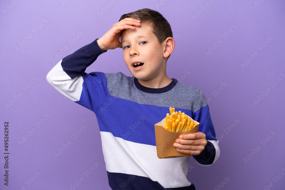 Little boy holding fried chips isolated on purple background doing surprise gesture while looking to the side Little boy holding fried chips isolated on purple background doing surprise gesture while looking to the side
