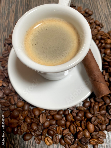 Closeup of espresso cup with foam and a cigar on plate and coffee roasted beans on wooden table
