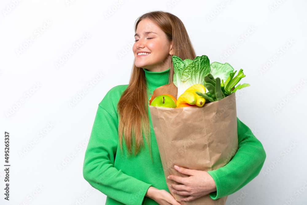 Young caucasian woman holding a grocery shopping bag isolated on white background laughing in lateral position Young caucasian woman holding a grocery shopping bag isolated on white background laughing in lateral position