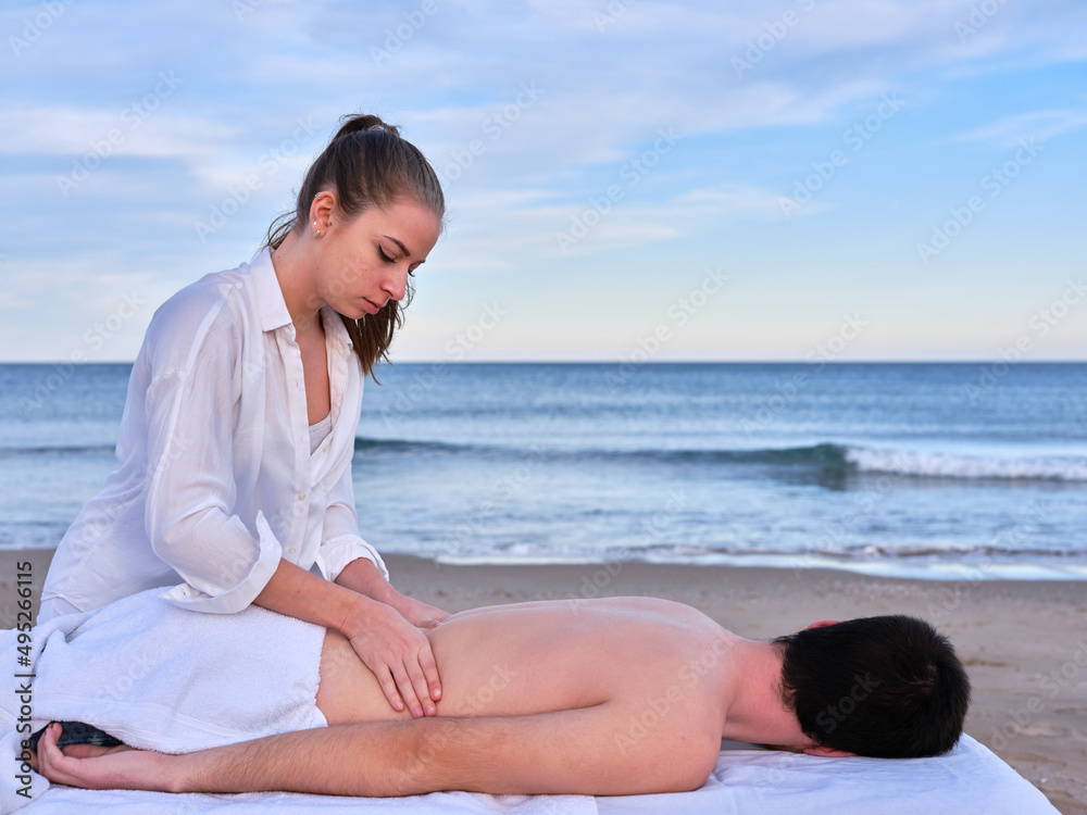 A young chiromassage therapist treating a lower back injury with massage and alternative medicine on a beach in Valencia.