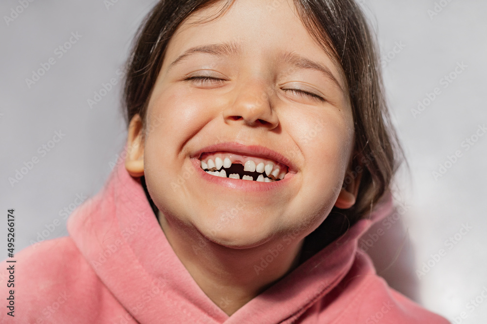 portrait of a beautiful emotional caucasian girl in a pink sweatshirt who lost her first tooth. Close-up of a child with a smile and joy portrait of a beautiful emotional caucasian girl in a pink sweatshirt who lost her first tooth. Close-up of a child with a smile and joy