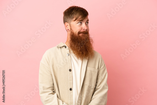 Young reddish caucasian man isolated on pink background having doubts while looking up © luismolinero