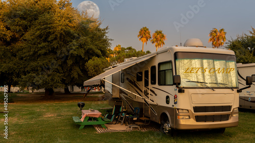 Sun begins to rise on the campsite with the moon setting behind the tree in the early morning