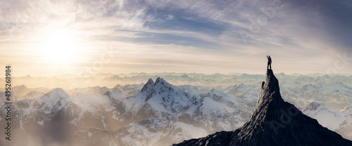 Adventurous Man Hiker standing on top of icy peak with rocky mountains in background. Adventure Composite. 3d Rendering rocks. Aerial Image of landscape from British Columbia, Canada. Sunset Sky photo