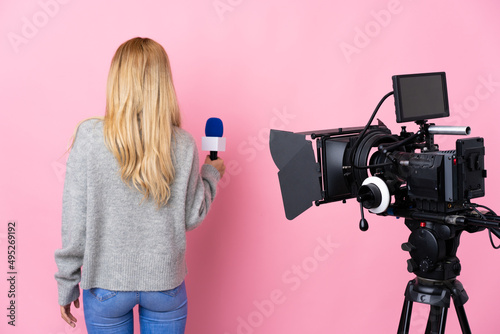 Fotografie Reporter woman holding a microphone and reporting news over isolated pink backgr