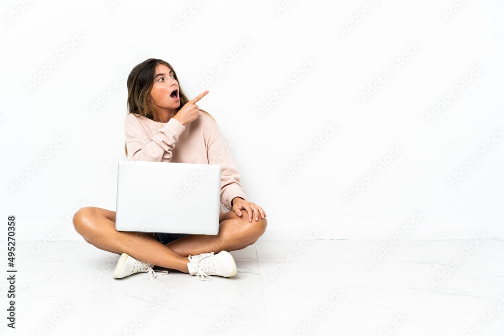 Young woman with a laptop sitting on the floor isolated on white background pointing away Young woman with a laptop sitting on the floor isolated on white background pointing away