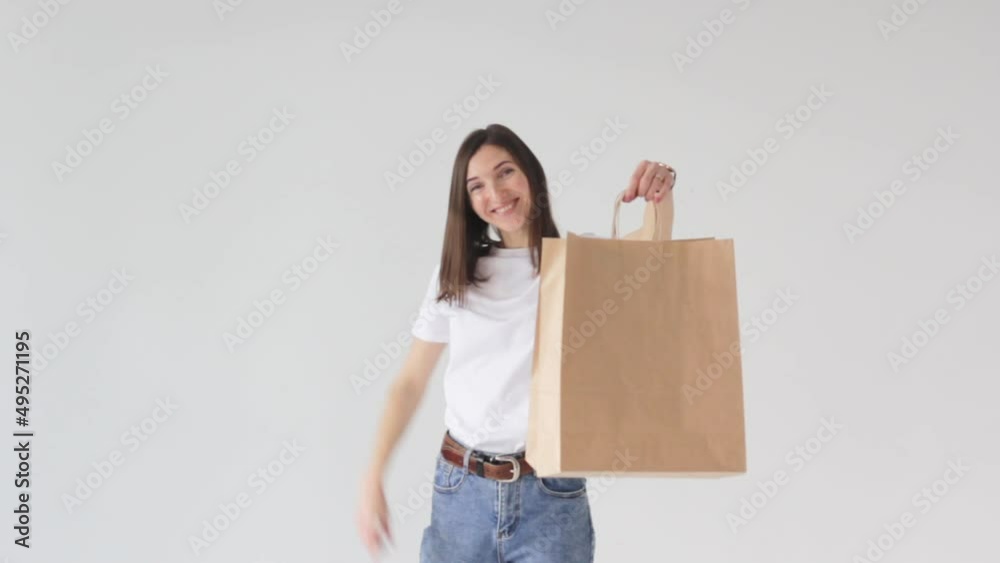 a beautiful young shopaholic girl with a paper bag on a white background points her finger at the package and smiles. a beautiful young shopaholic girl with a paper bag on a white background points her finger at the package and smiles.