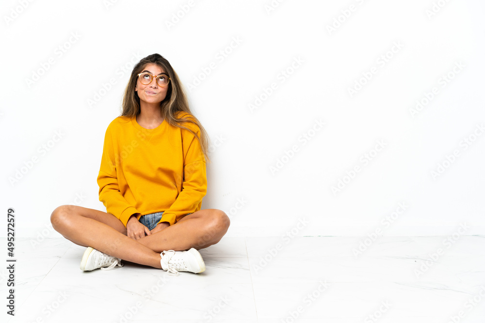 Young woman sitting on the floor isolated on white background and looking up