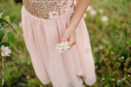 Little girl wearing light pink dress holding blooming apple tree flowers.