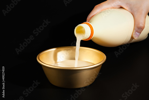 Makgeolli rice wine is a Korean fermented alcoholic beverage traditional drinks. 
Korean alcoholic drink (Makgeolli) in a traditional Korean gold liquor bowl with snack on Black background. 