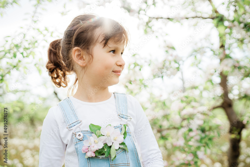 Little girl dressed in denim overalls, apple tree flowers in a pocket, blooming branch of an apple tree Little girl dressed in denim overalls, apple tree flowers in a pocket, blooming branch of an apple tree