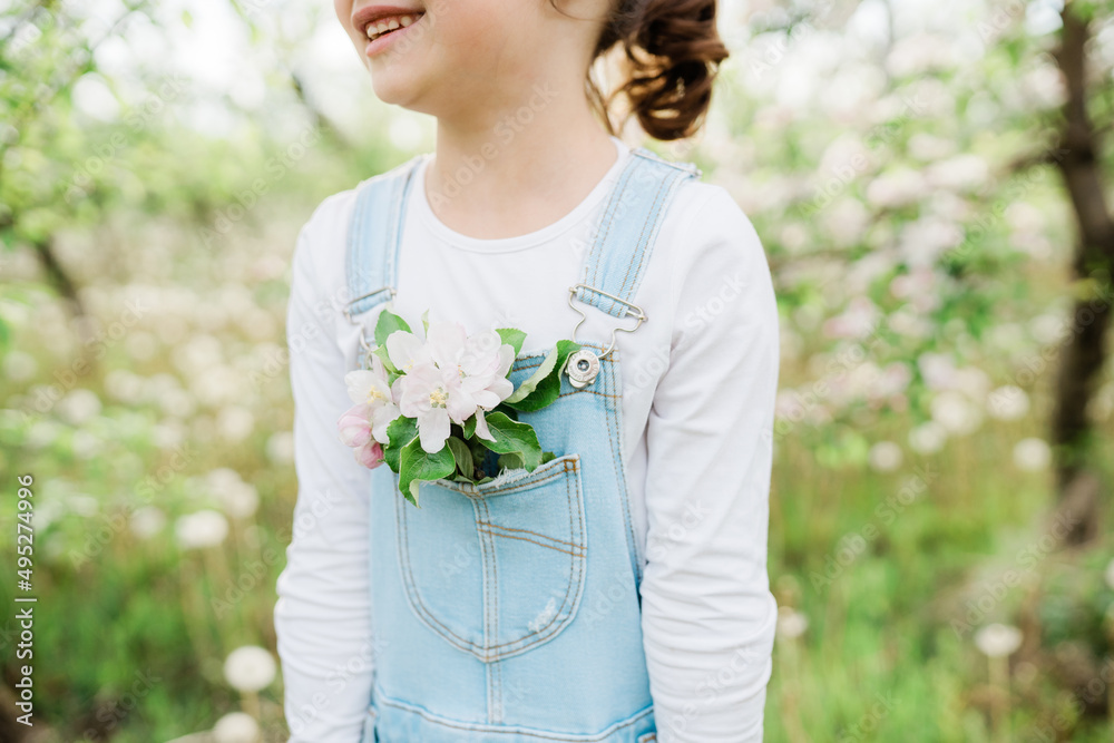 Little girl dressed in denim overalls, apple tree flowers in a pocket, blooming branch of an apple tree Little girl dressed in denim overalls, apple tree flowers in a pocket, blooming branch of an apple tree