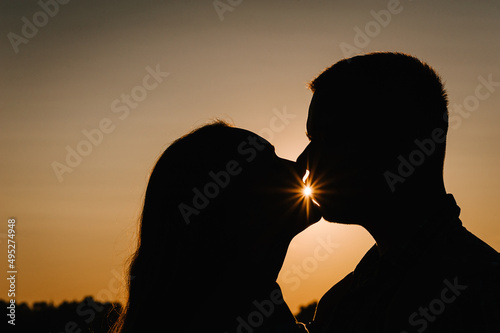 Silhouette of a couple. Young couple kissing at sunset in spring. A man and woman on background of sun. Concept of love and family. Close Up.