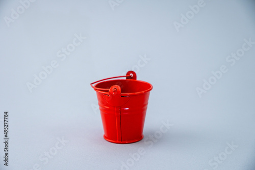 Red small iron bucket on a gray background. Children's red bucket. Gardening tools. Close-up. Selective focus. Gardening concept.Micro gardening. Home small garden tools for growing micro greens. © Василь Івасюк