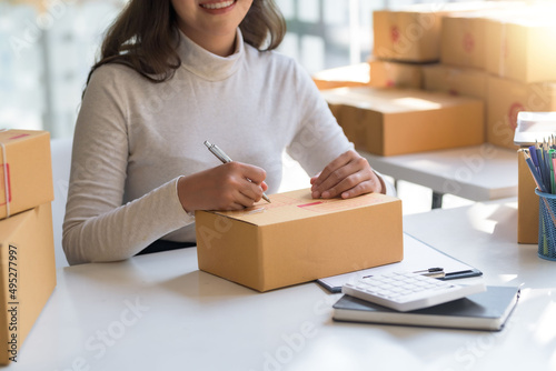 Online sales business owner woman is taking note of the customer's address on the parcel box being prepared for delivery. © amnaj
