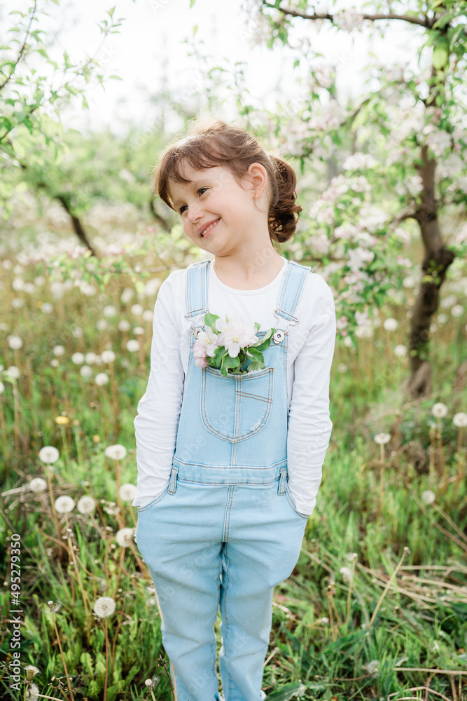 Little girl dressed in denim overalls, apple tree flowers in a pocket, blooming branch of an apple tree Little girl dressed in denim overalls, apple tree flowers in a pocket, blooming branch of an apple tree