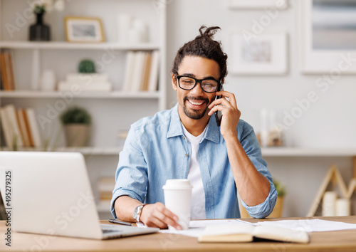 Positive black freelancer talking on smartphone at home