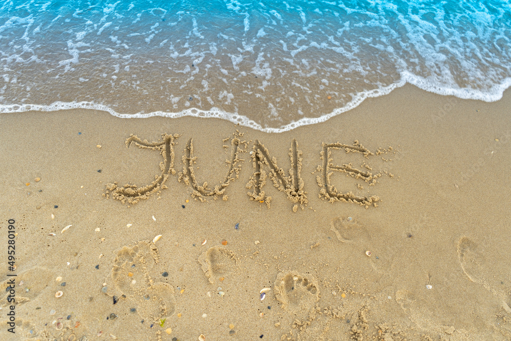 Fototapeta premium The word June is written on the sand of a beach by the sea. Washed off by a wave. The inscription disappears. End of summer concept. Back to school