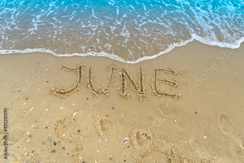 Fototapeta Naklejka Na Ścianę i Meble -  The word June is written on the sand of a beach by the sea. Washed off by a wave. The inscription disappears. End of summer concept. Back to school