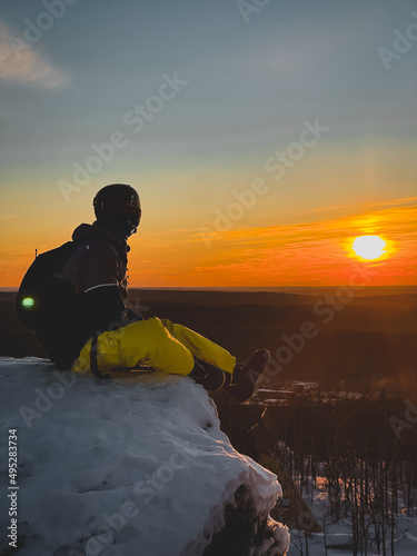 Snowboarder sit edge mountain, looks into the distance against backdrop sunset