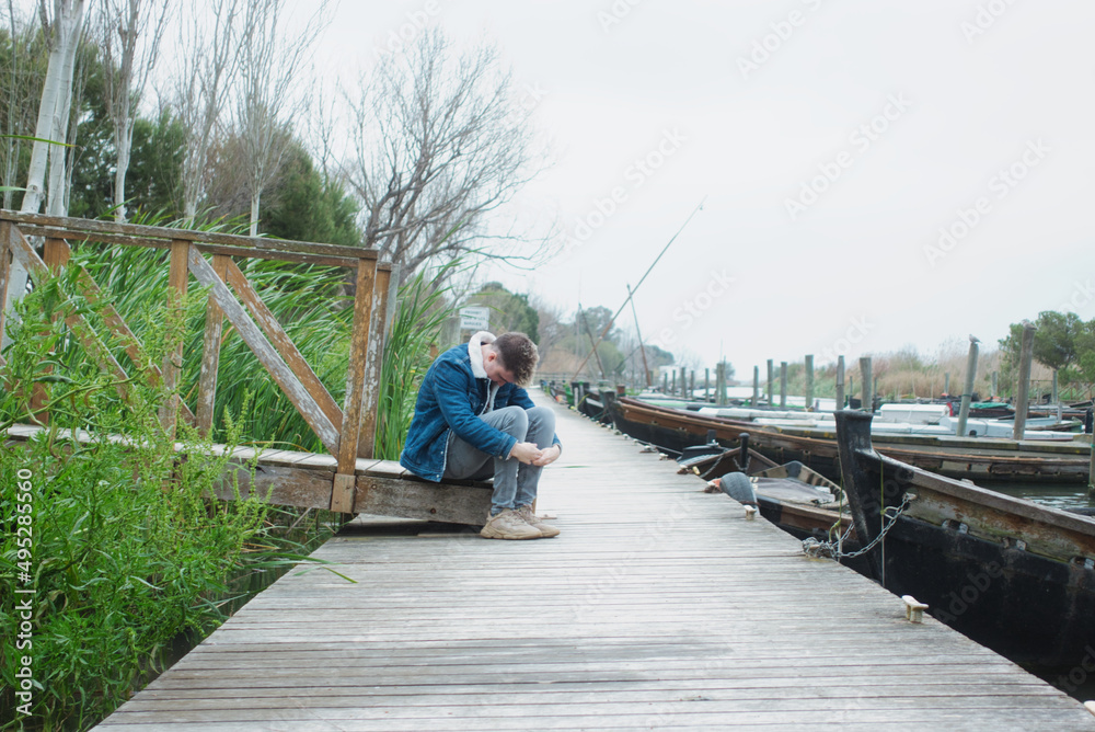 Concept of depression and anxiety of man in fetal position on the jetty of a lake. Copy space.