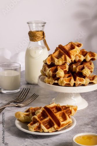 Table setup with a pile of croffles on a stand, paired with milk, syrup, and silverware. photo