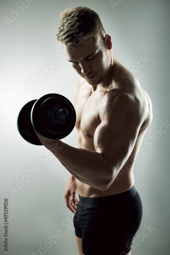Weights before dates. Studio shot of a muscular young man exercising with a dumbbell against a grey background.