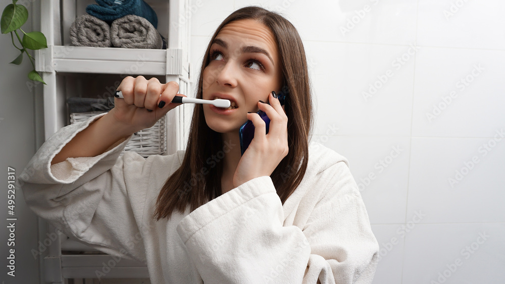 Busy young woman brushing teeth and talking on the phone simultaneously. Businesswoman late for work. Morning multitasking in the bathroom.
Busy young woman brushing teeth and talking on the phone simultaneously. Businesswoman late for work. Morning multitasking in the bathroom.