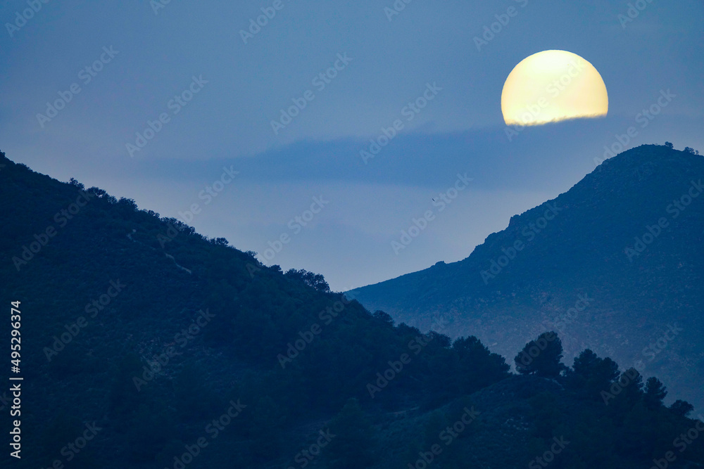 Fototapeta premium Sun disk between mountains at sunset