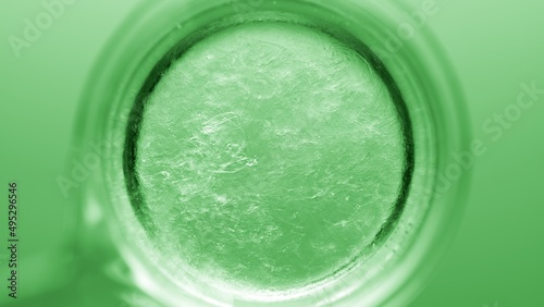 Top view macro shot of glycerin being poured into beaker with water creating solution on green background | Abstract cosmetics formulation concept