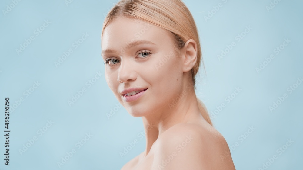 Beauty portrait of young slim gorgeous European blond woman who looks at the camera over her shoulder on blue background with water ripples | Beauty care and skin moisturizer commercial concept Beauty portrait of young slim gorgeous European blond woman who looks at the camera over her shoulder on blue background with water ripples | Beauty care and skin moisturizer commercial concept