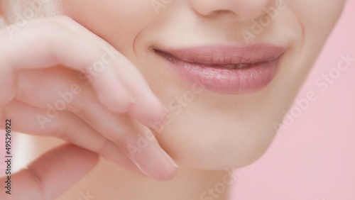 Extreme close-up of pretty female beauty model touches her face skin with her hand smiling on pink background | Perfect skin and beauty care concept