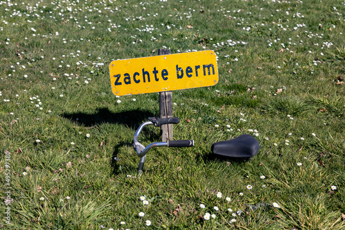 Warning sign says soft roadside in dutch and a sunken bike photo