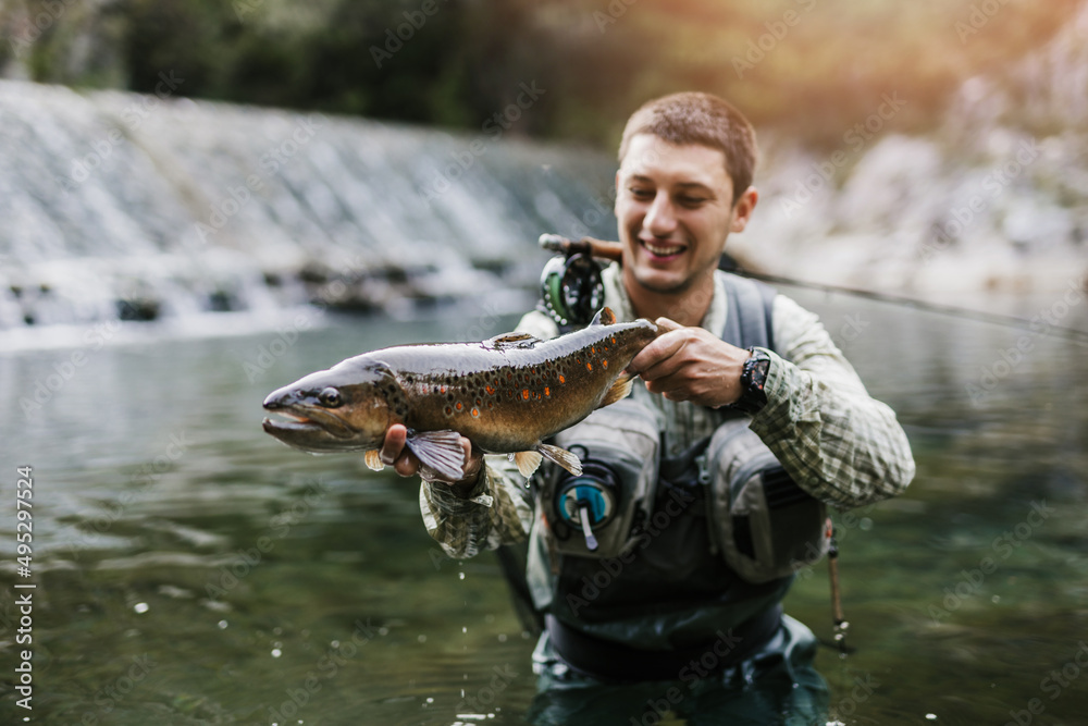 Man, who does sports fishing, fishes on a fast mountain river and holds a trout she caught in his hand. Man, who does sports fishing, fishes on a fast mountain river and holds a trout she caught in his hand.