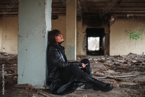Young woman in leather coat alone in a destroyed residential building, loneliness and despair in abandoned city