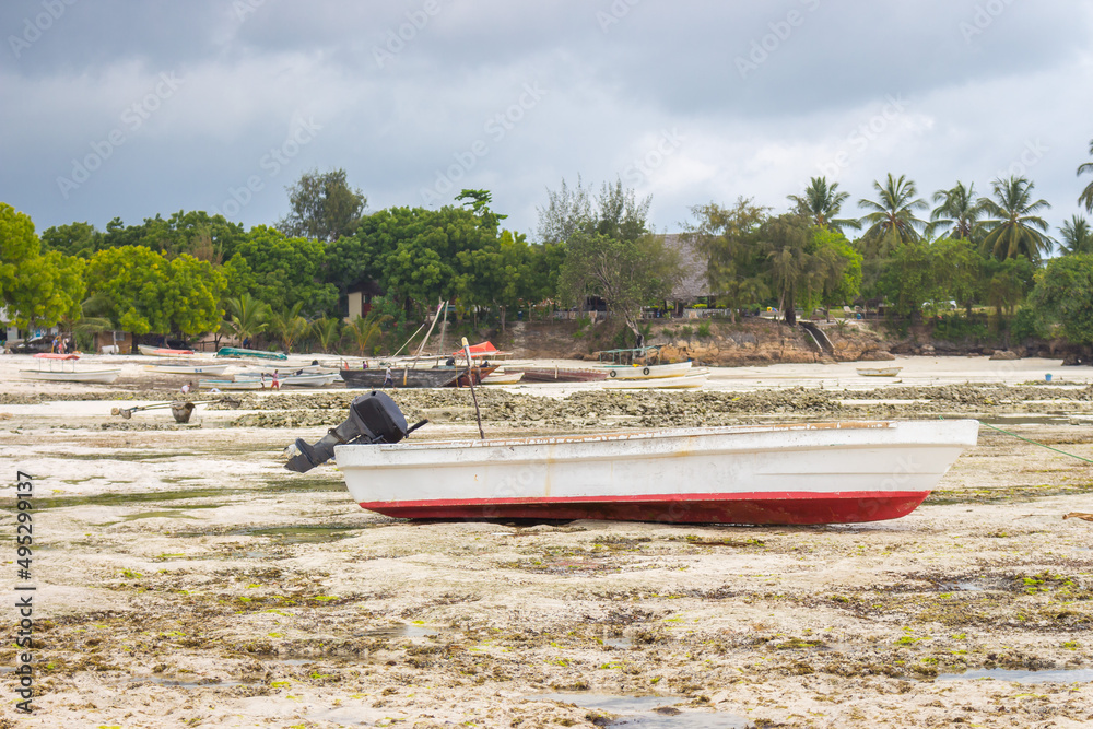 Obraz premium White fishing boat on the beach on tropical background. Sailboats at seaside. Low tide in lagoon. Exotic nature. Nautical vessel on coastline with palm trees. Indian Ocean coast with boats.