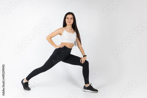 Fitness girl doing stretching workout on white background. Attractive brunette woman in fashionable sportswear exercising. Healthy lifestyle, sport concept, Full length view