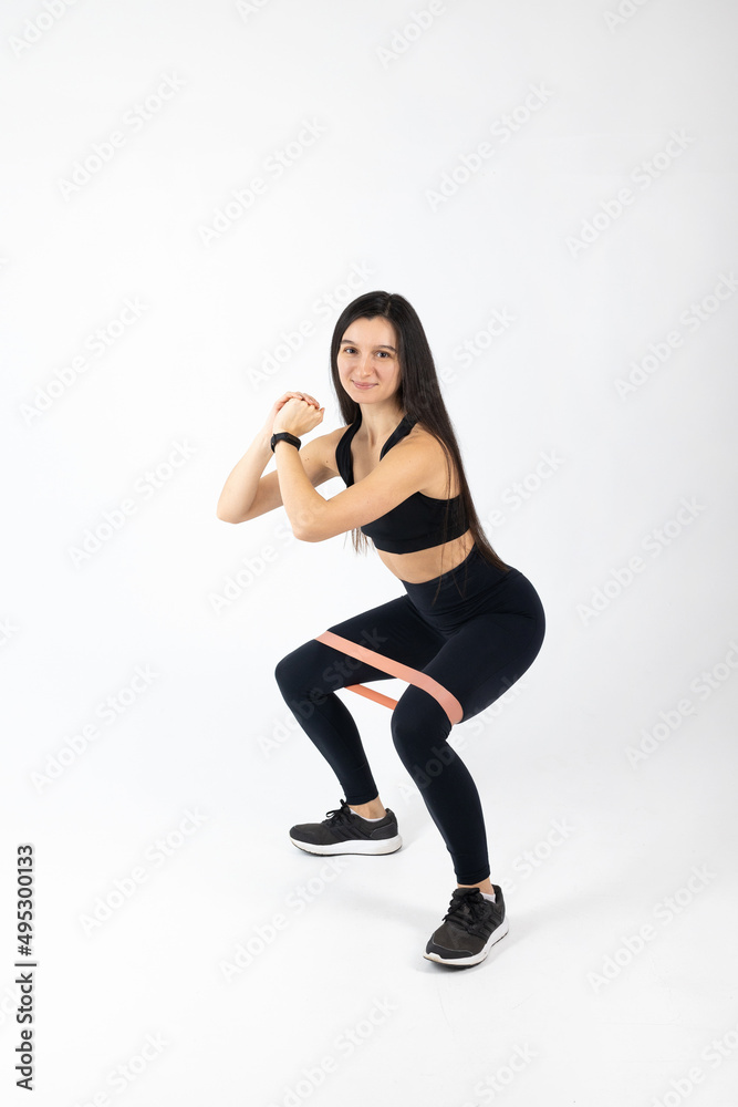 Sportswoman exercising with resistance band on white background. Attractive brunette woman in fashionable sportswear exercising. Healthy lifestyle, sport concept, Full length view