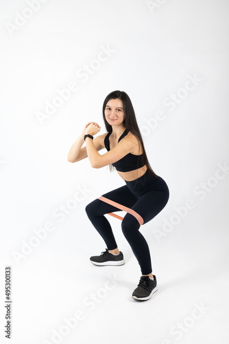 Sportswoman exercising with resistance band on white background. Attractive brunette woman in fashionable sportswear exercising. Healthy lifestyle, sport concept, Full length view