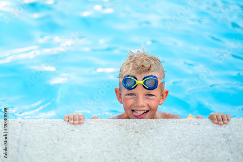 Portrait smiling boy in swimming pool, child in swimming glasses and inflatable sleeves. Summer travel hotel vacation or classes