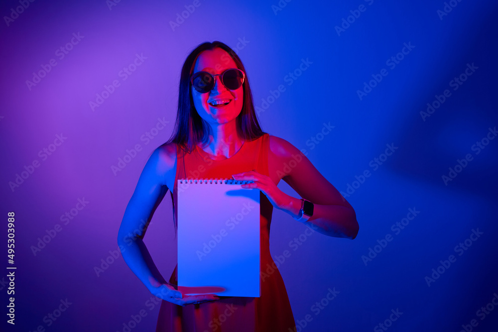 happy girl showing blank paper notebook in neon lights happy girl showing blank paper notebook in neon lights