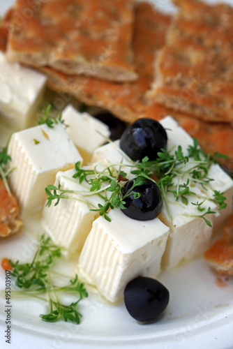 Feta cheese with microgreens, olives and crackers. Healthy snack or snack. White cheese with olive oil.